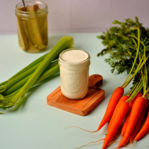 A jar of dressing with carrots and celery next to it.