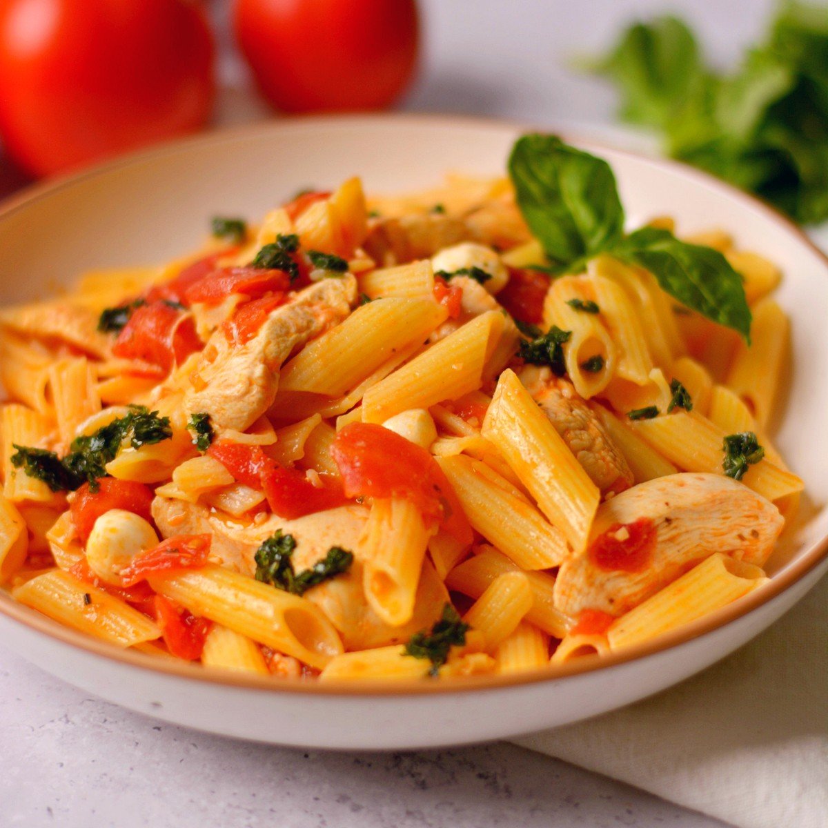 Penne pasta, tomatoes, and basil in a white bowl.