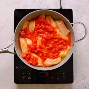 Chicken pieces and tomatoes cooking in a skilet.