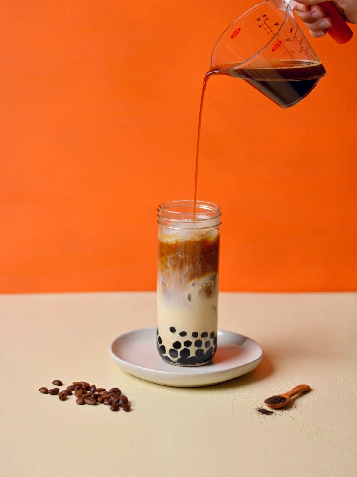 Pouring coffee into a glass with boba, ice and milk.