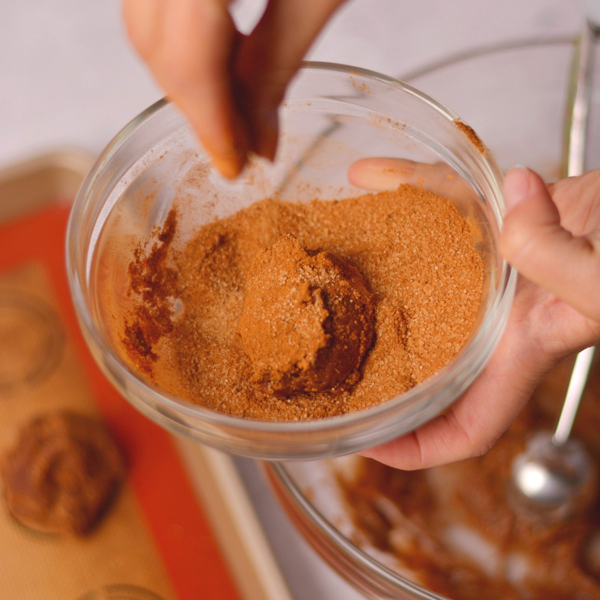 Sprinkling cinnamon sugar on a ball of cookie dough.