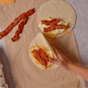 Folding a tortilla in half filled with bacon, egg and cheese.