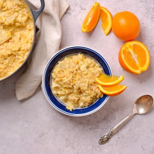 Orange risotto in a bowl with a pot of risotto next to it.