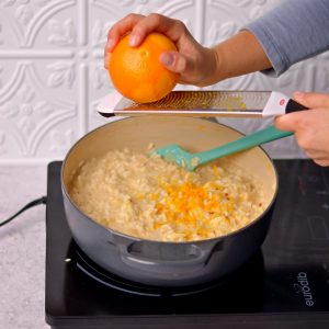 Zesting and orange into a pot filled with rice.