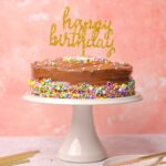 Chocolate Coffee birthday cake on a cake stand with a happy birthday sign.