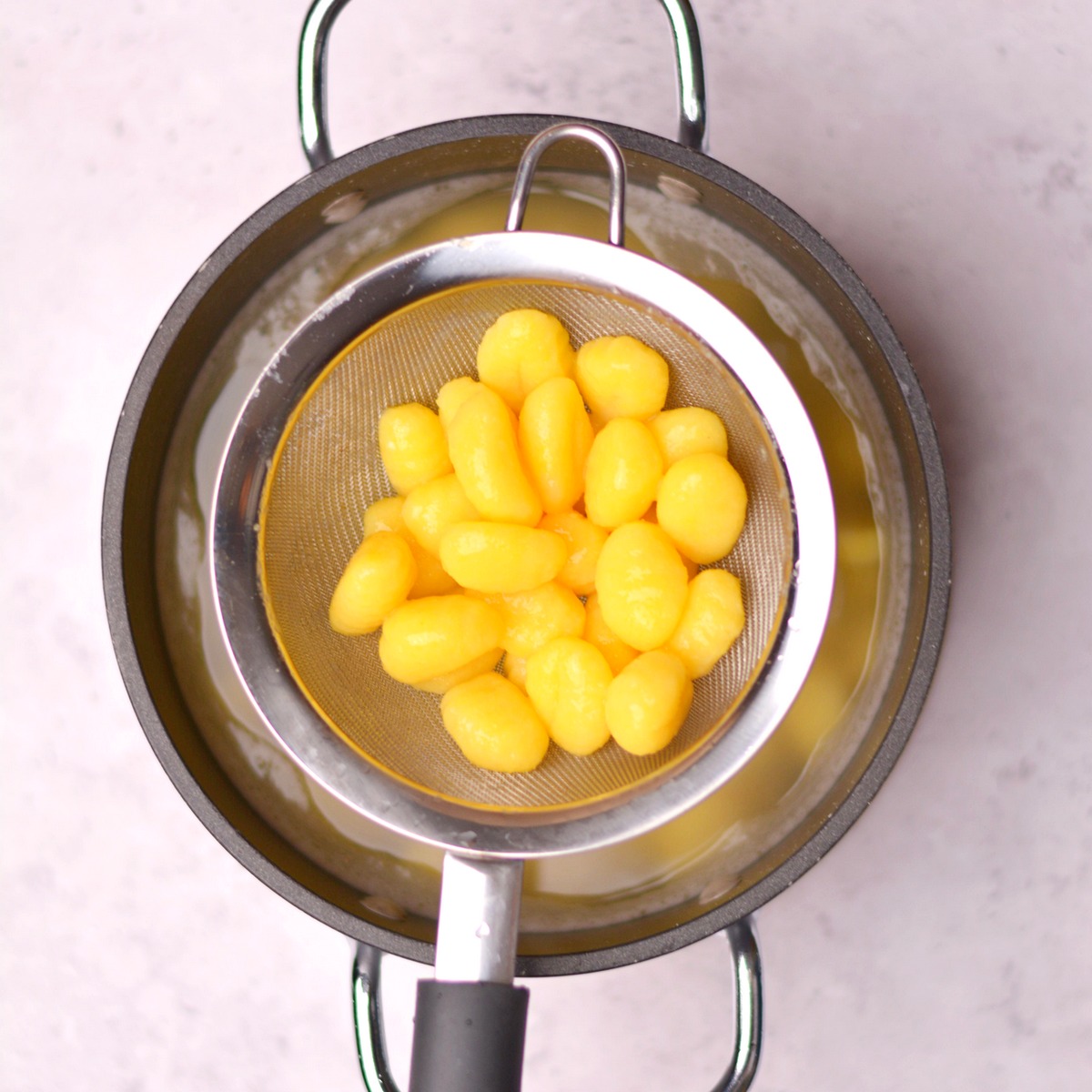Gnocchi in a strainer on top of a pot.
