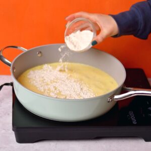 Adding flour to a skillet with a butter sauce.
