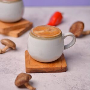 Chaga mushroom latte in a mug surrounded by mushrooms and a chili pepper.