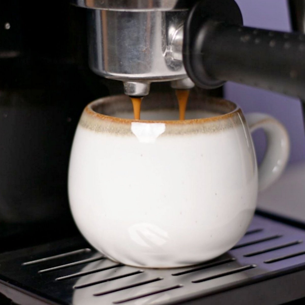 Cup under espresso maker while espresso brews into cup.