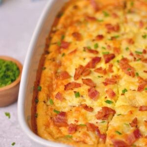 An egg bake in a white casserole dish with bacon and chives on top.