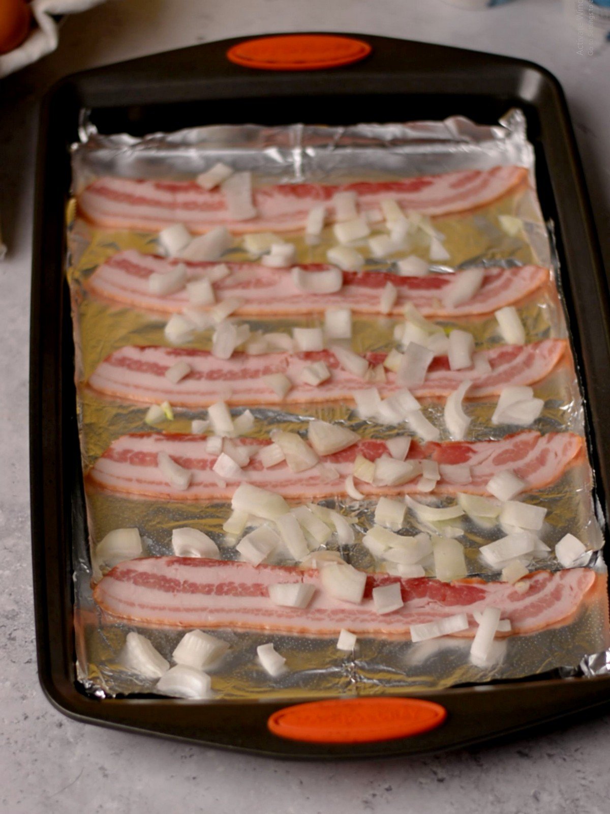 Bacon and diced onions on a baking tray lined with aluminum foil.