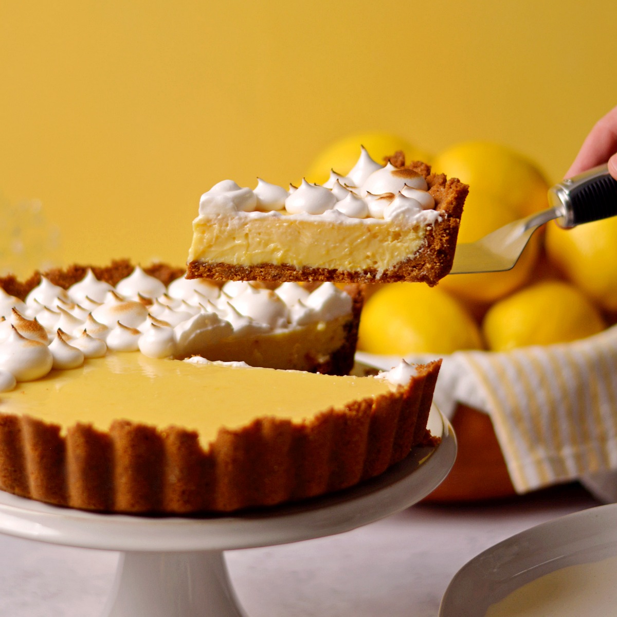 Taking a piece of lemon meringue pie from a pie on a white stand.