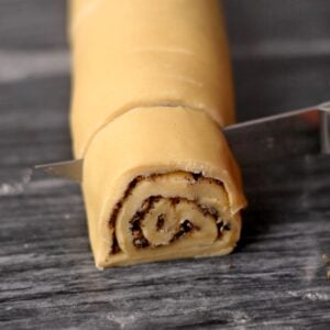 Slicing rolled up cinnamon roll dough with a knife.