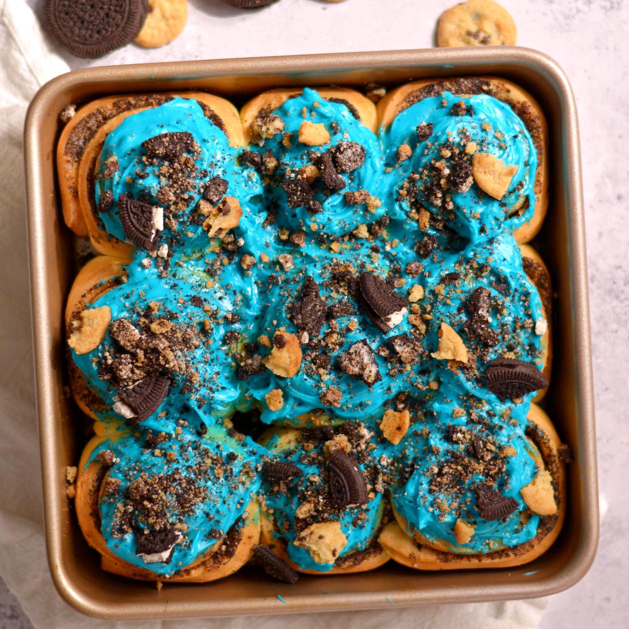 Cookie monster cinnamon rolls in a square pan with blue frosting and crushed cookies on top.