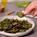 Picking up a piece of crispy spinach from a plate full of spinach.