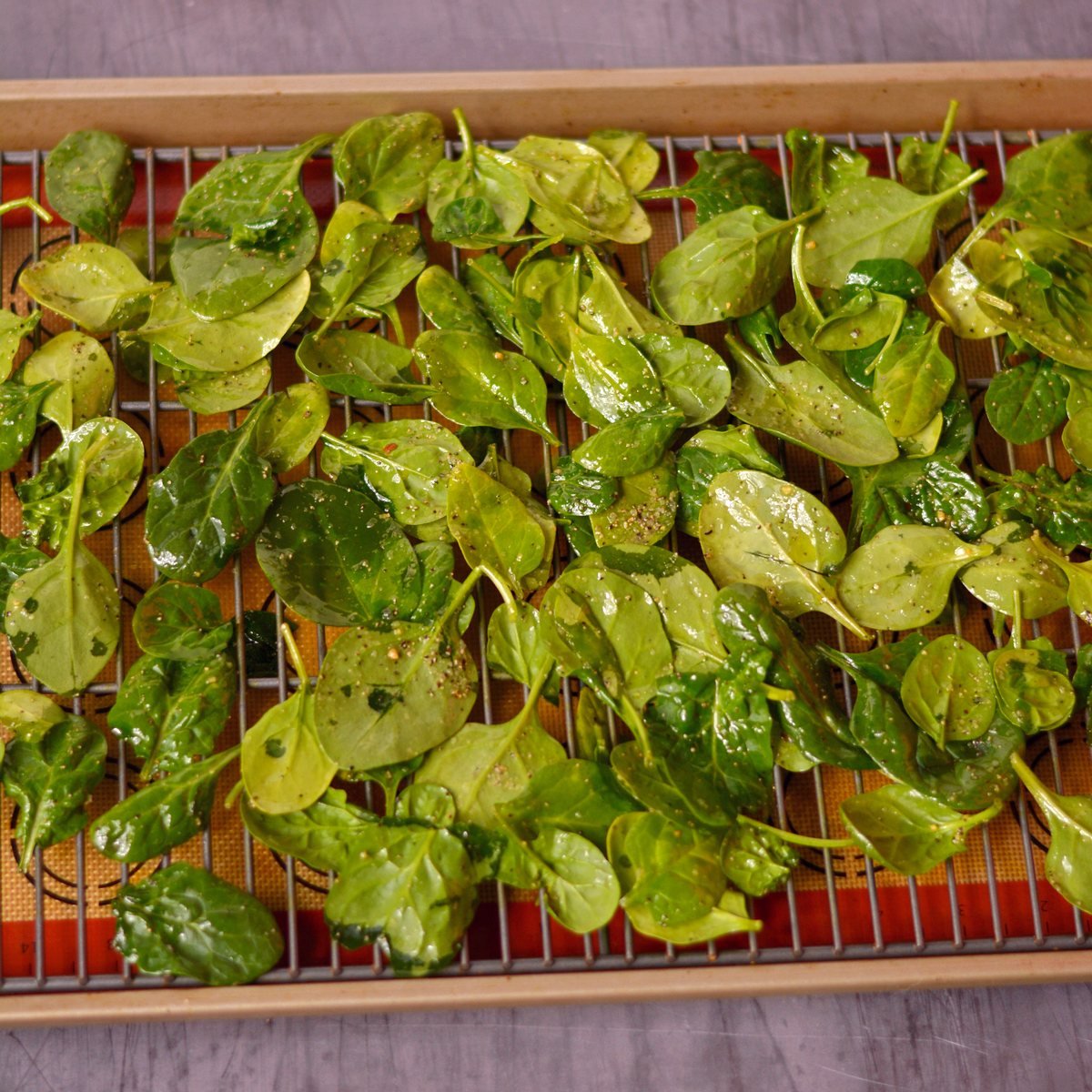 Spinach with oil and seasoning on a wire rack on a baking sheet.