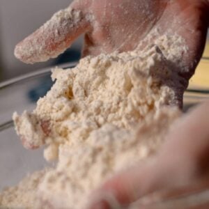 Two hands mixing flour and butter in a bowl.