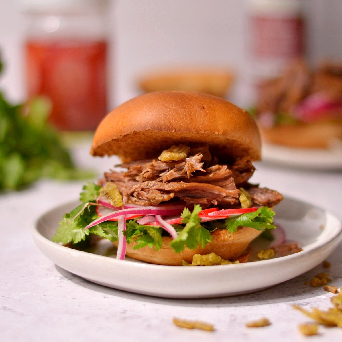 A pulled beef burger with leafy greens, red onions, and radishes on top.