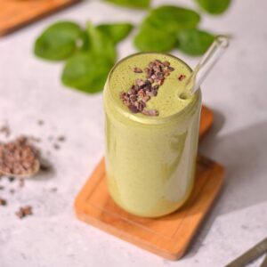 A green shake with cacao nibs in a glass with a glass straw.