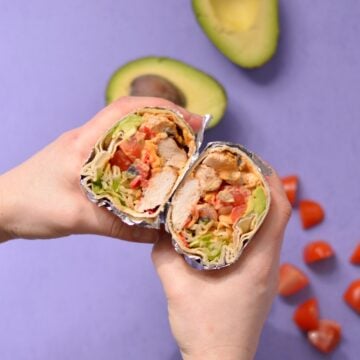 Burrito cut open to show the filling ingredients and being held by hands.