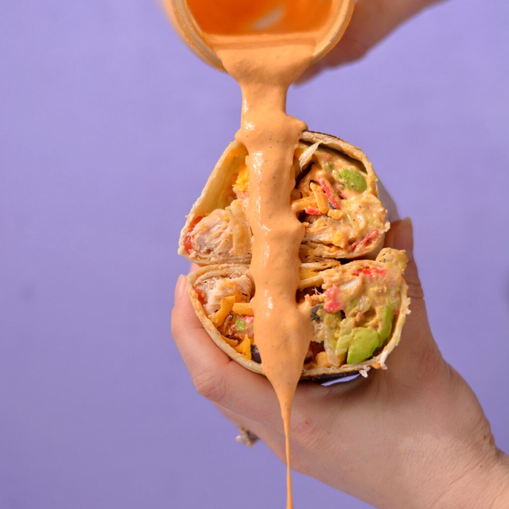 Chipotle ranch being poured over two cut open halves of a burrito.