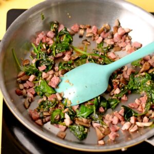 A pan with spinach, mushroom, and ham being sautéed.