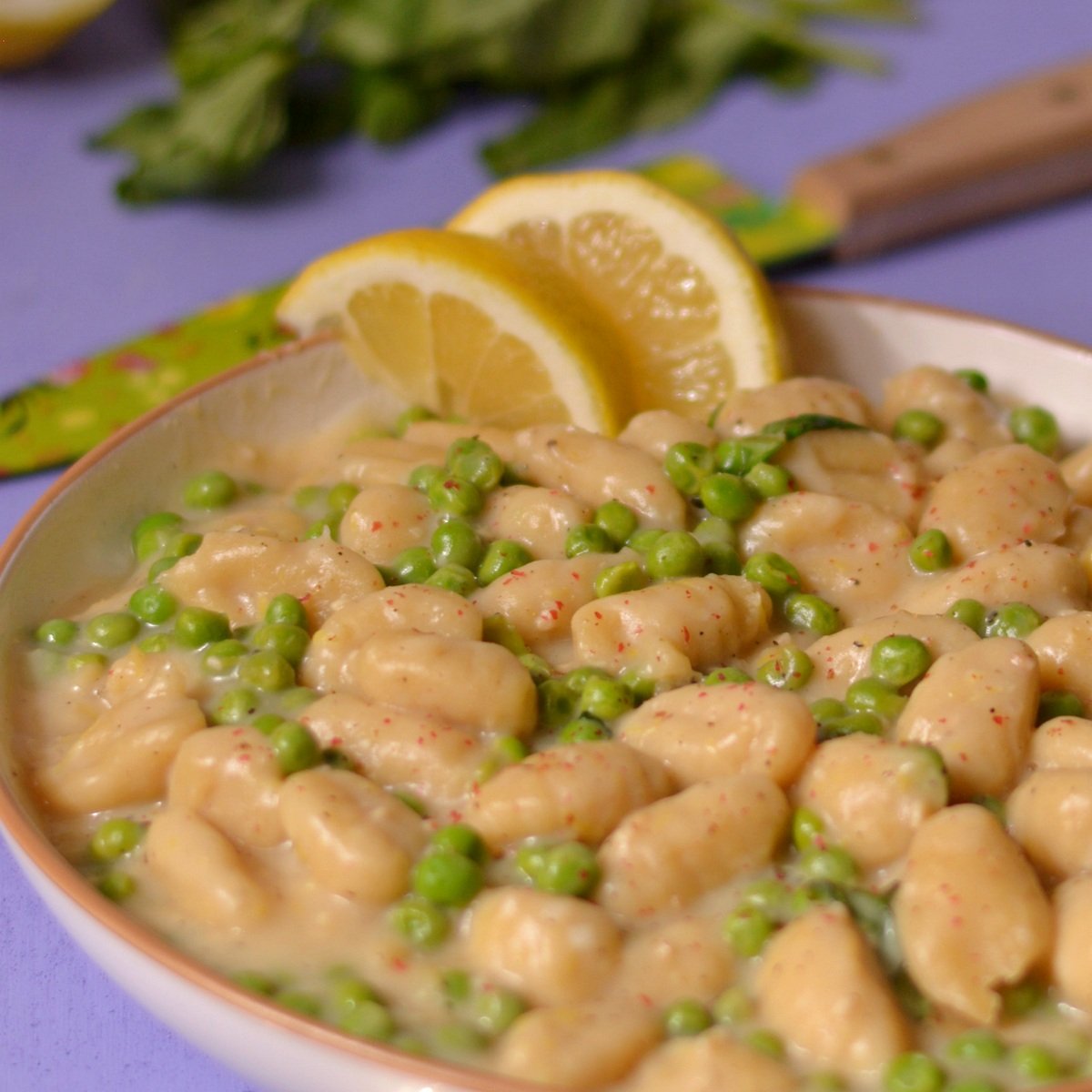 A bowl of gnocchi and peas with slices of lemon.