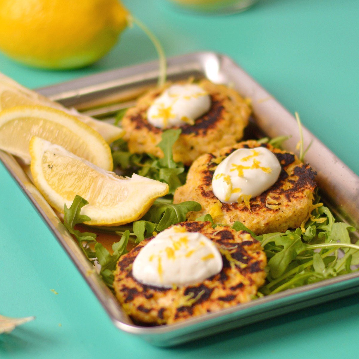 salmon patties on a tray with white sauce and lemons.