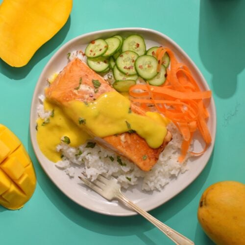 Overhead image of salmon on a plate with rice, cucumbers, carrots, and mango sauce.