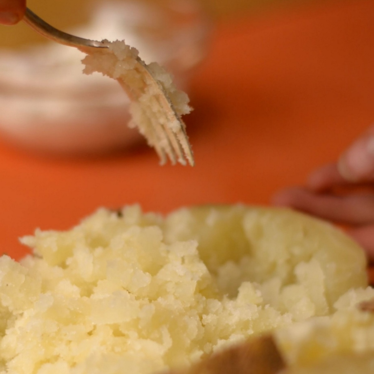 A fork fluffing and mashing the inside of a russet potato.