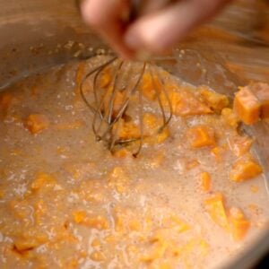 A whisk in an Instant Pot with sweet potato porridge.