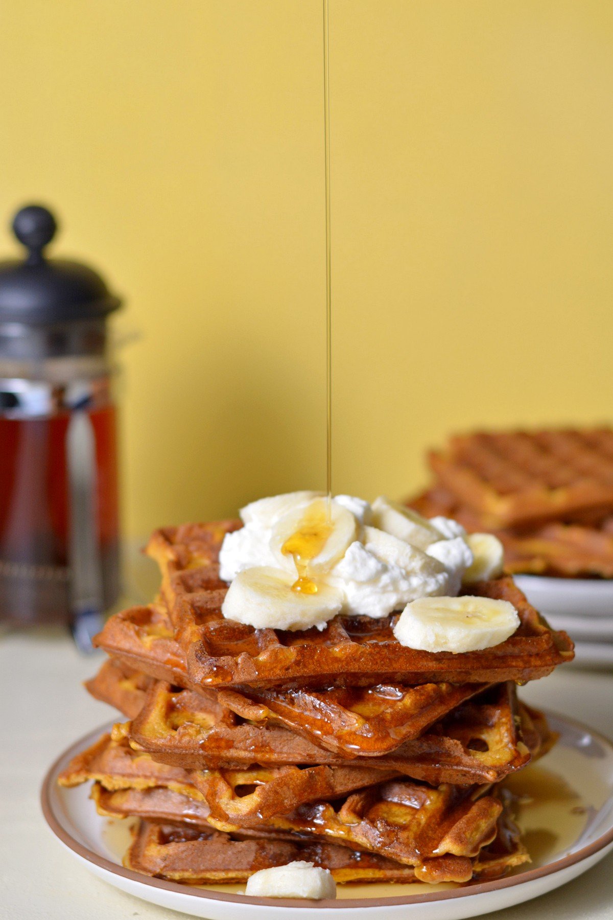 A stack of sweet potato waffles with whipped cream and banana slices on top.