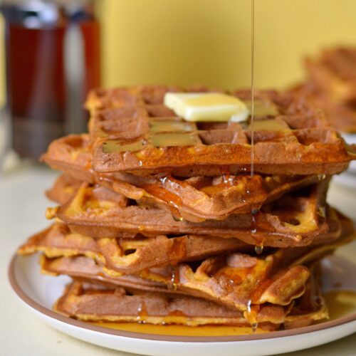 Pouring syrup on top of a stack of sweet potato waffles.