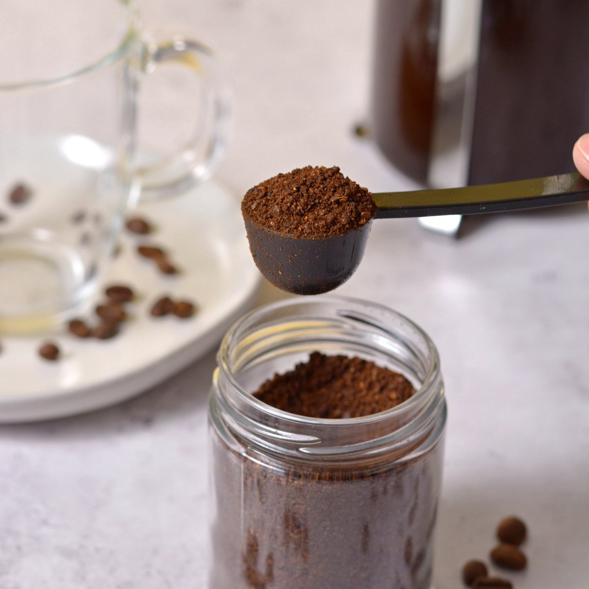 Taking a scoop of coffee grounds out of a glass jar.