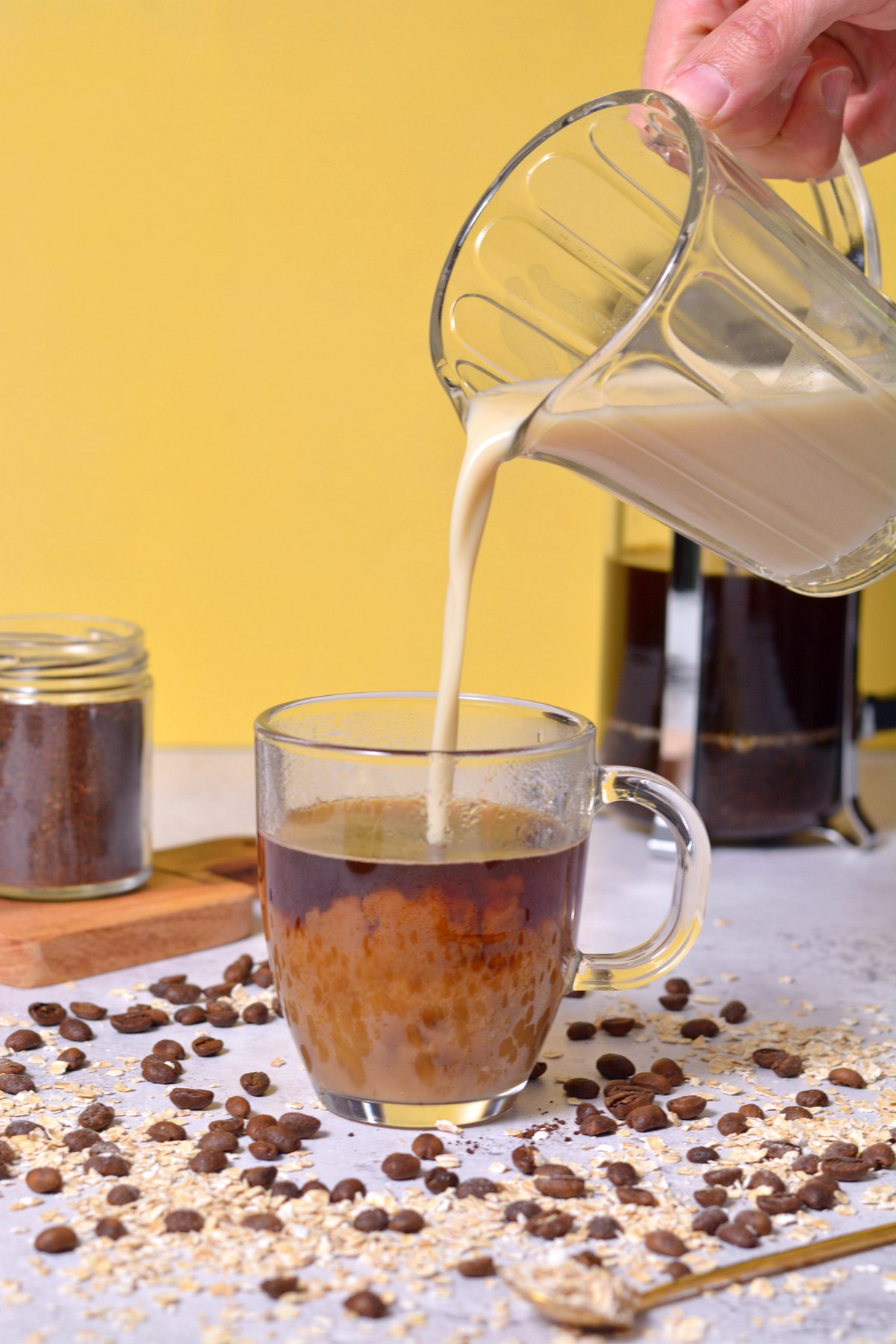 Pouring oat milk into a glass mug of coffee.