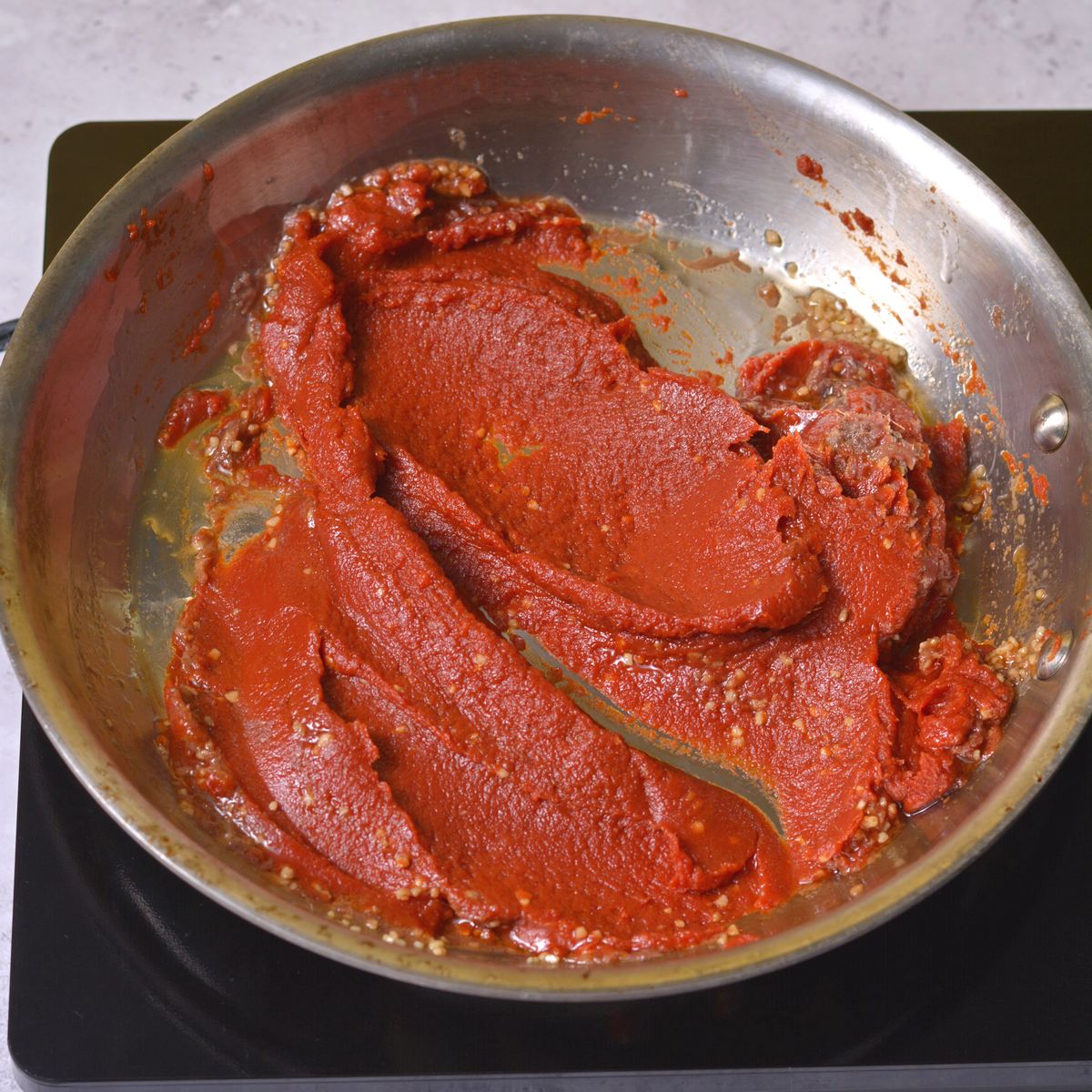 Cooking tomato paste and pesto ingredients in a pan.