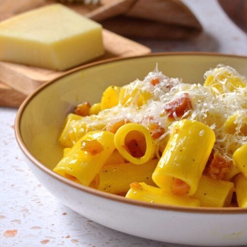 A shallow bowl of rigatoni carbonara with grated cheese on top.