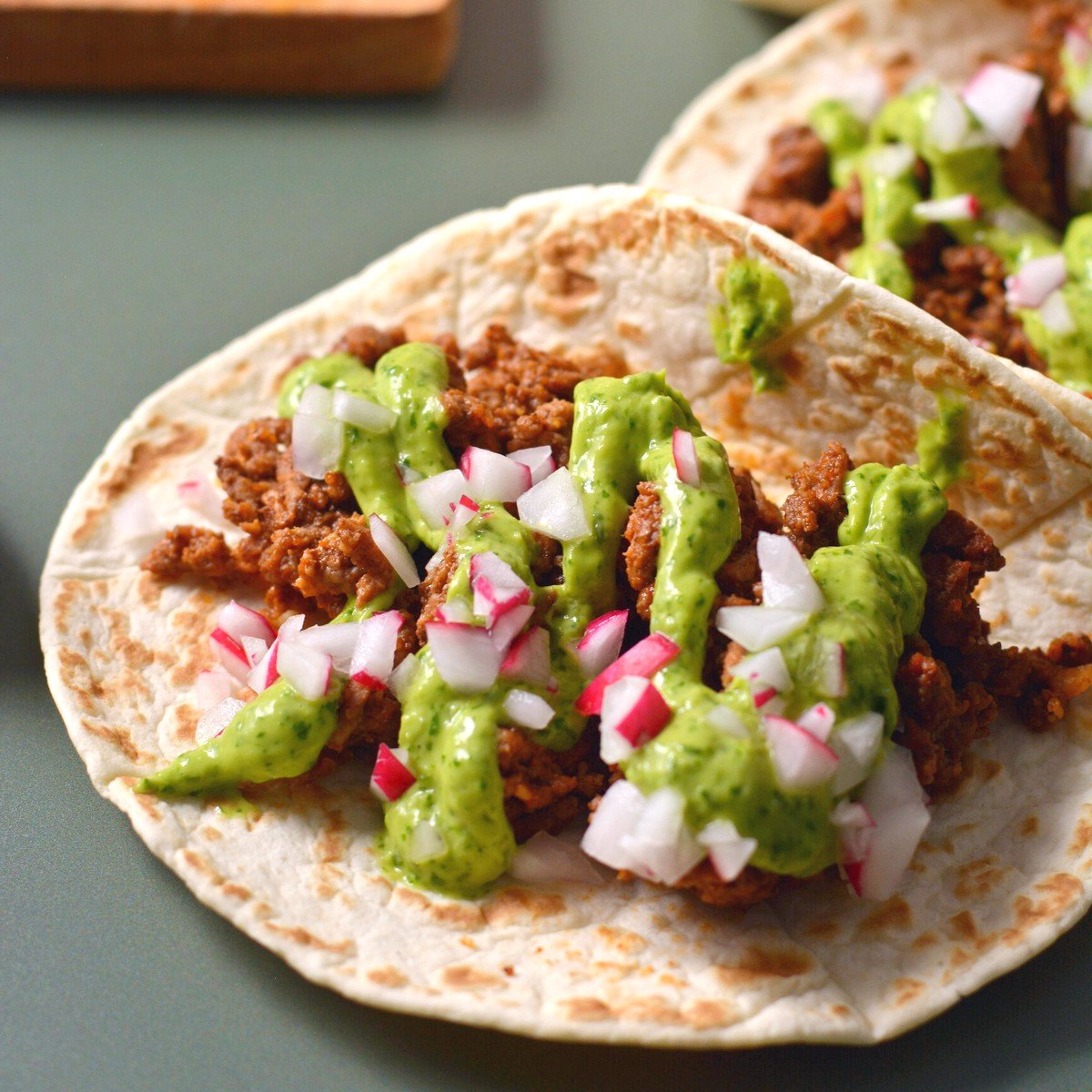 Ground bison tacos with radish pieces and green salsa.