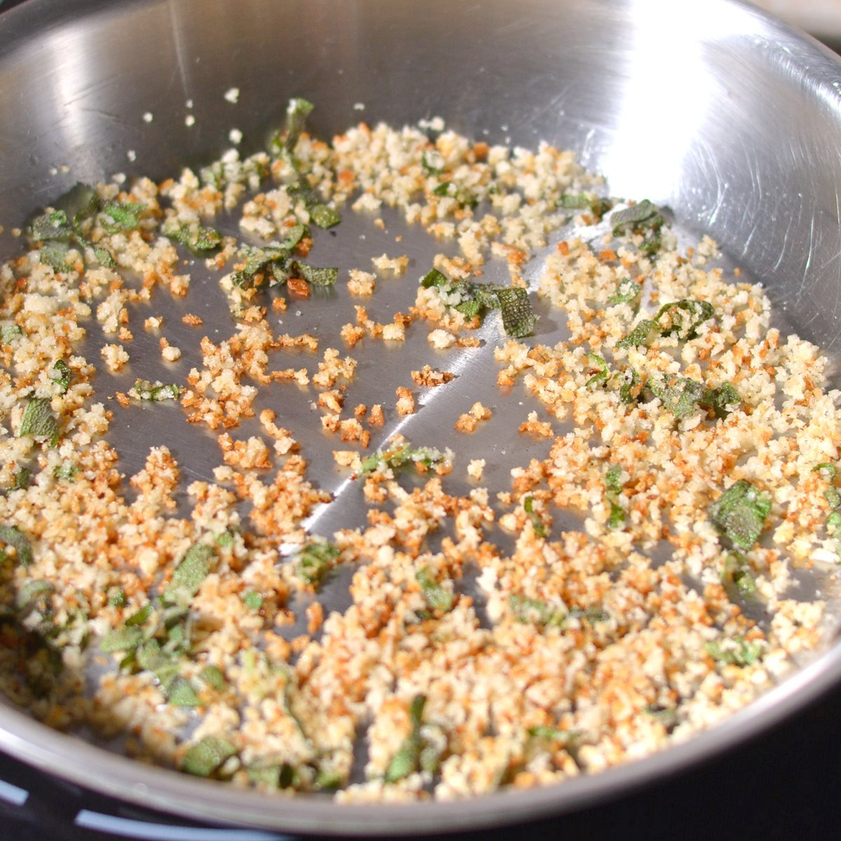 A skillet with toasted bread crumbs and sage leaves.