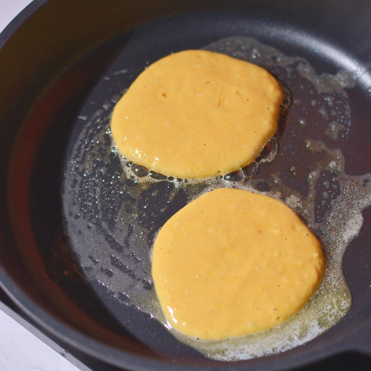 A pan with two pancakes on it before flipping.