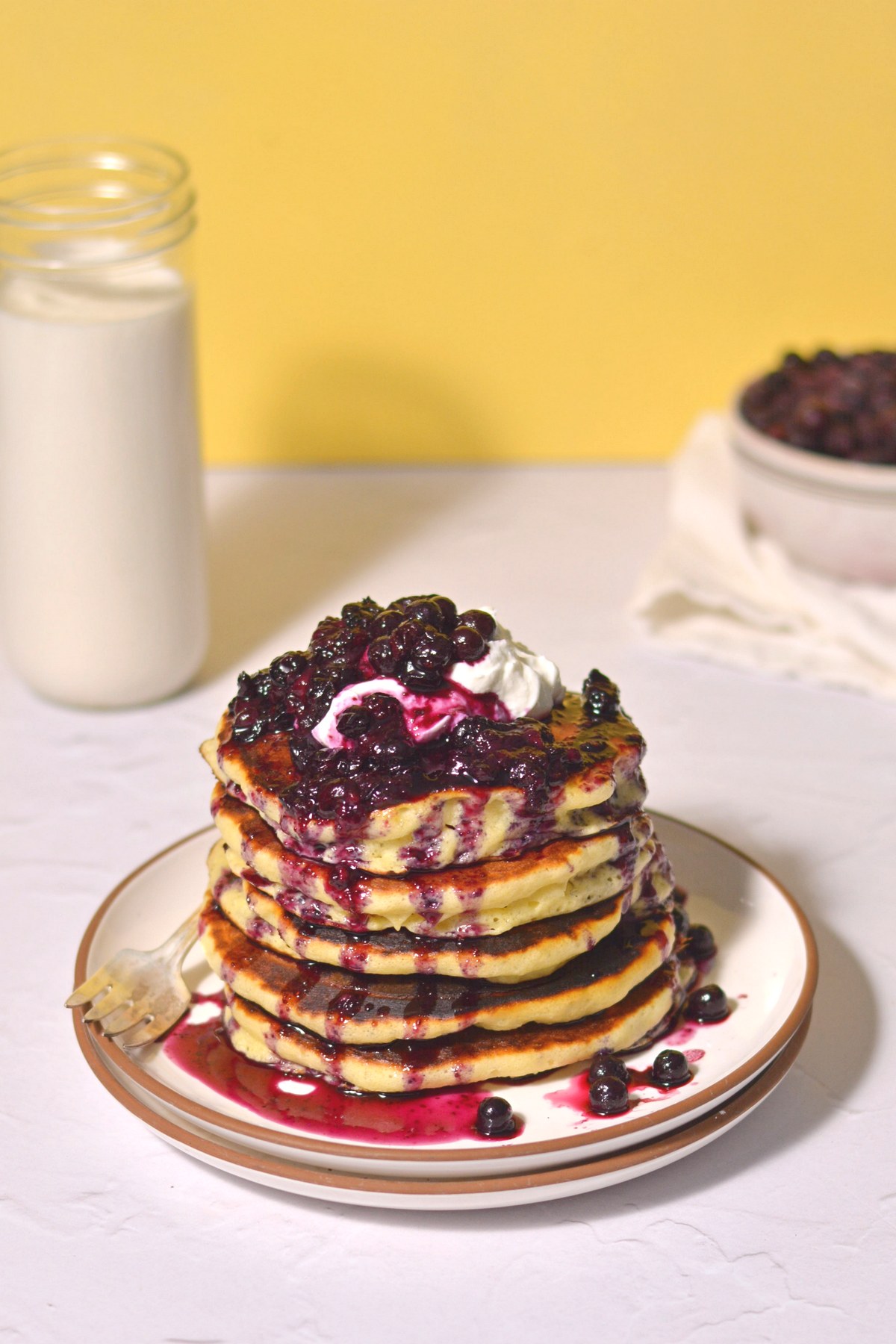 A stack of pancakes with blueberries dripping down the sides.