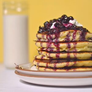 A stack of pancakes with blueberries on top in front of a yellow background.