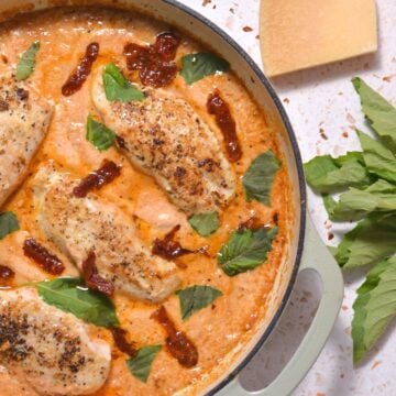 A pan filled with tuscan chicken, sauce, basil leaves, and sun dried tomatoes.