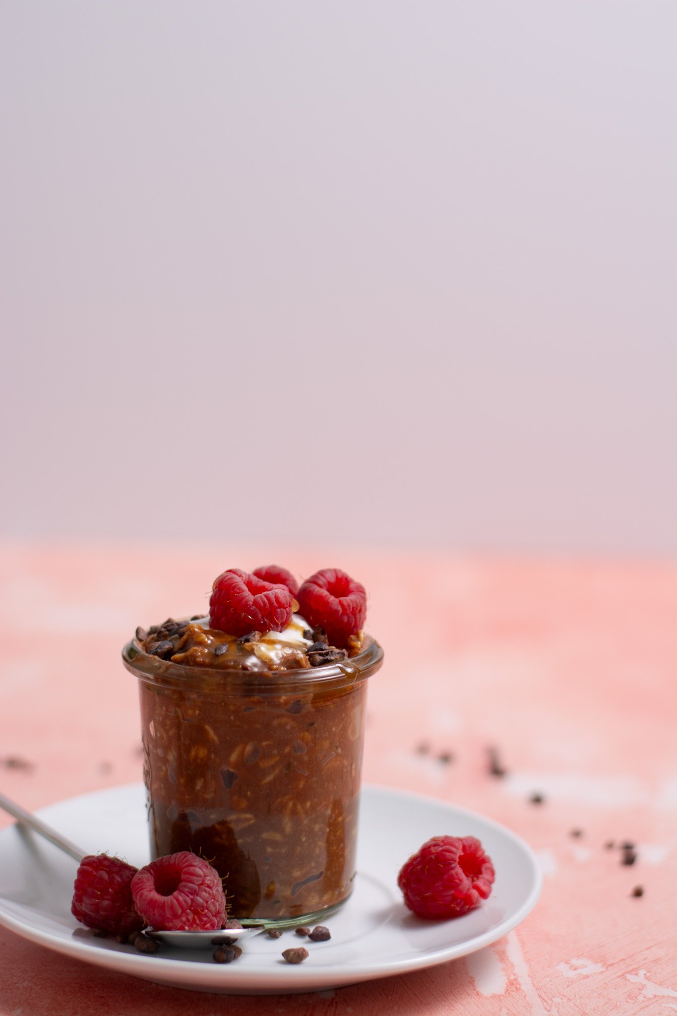 brownie batter protein overnight oats in a jar with raspberries on top and a white bowl behind.