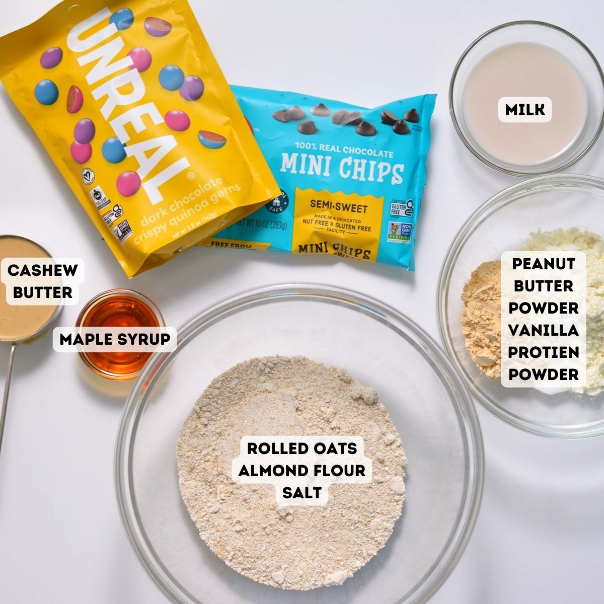 Ingredients including m and m's, chocolate chips, oats, almond flour, cashew butter, maple syrup, milk, peanut butter powder, and protein powder.