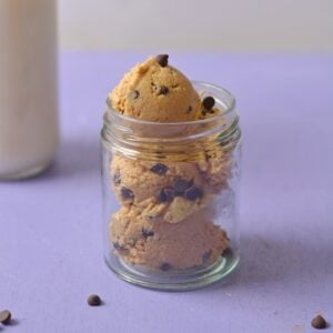 Protein cookie dough in a glass jar on a purple background.