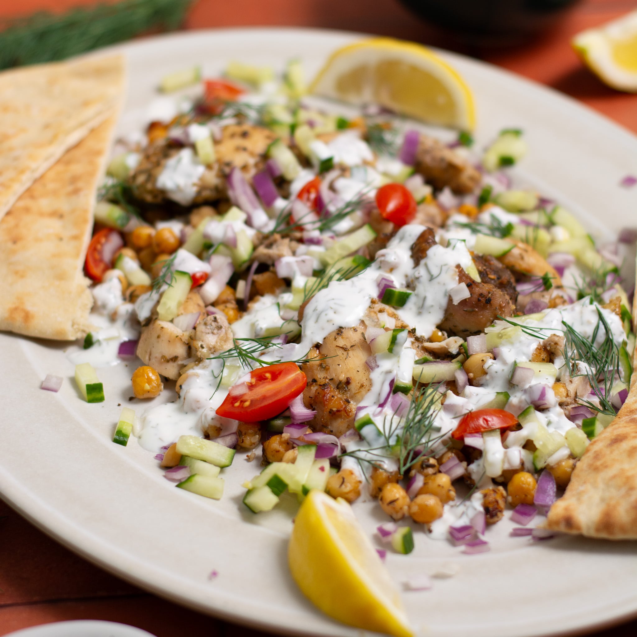 Sheet pan chicken gyros on a serving tray with yogurt sauce on top.