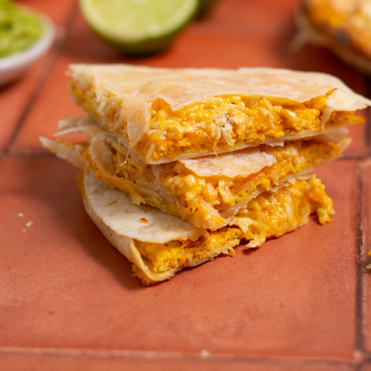 A stack of protein breakfast quesadillas on a red tile background.