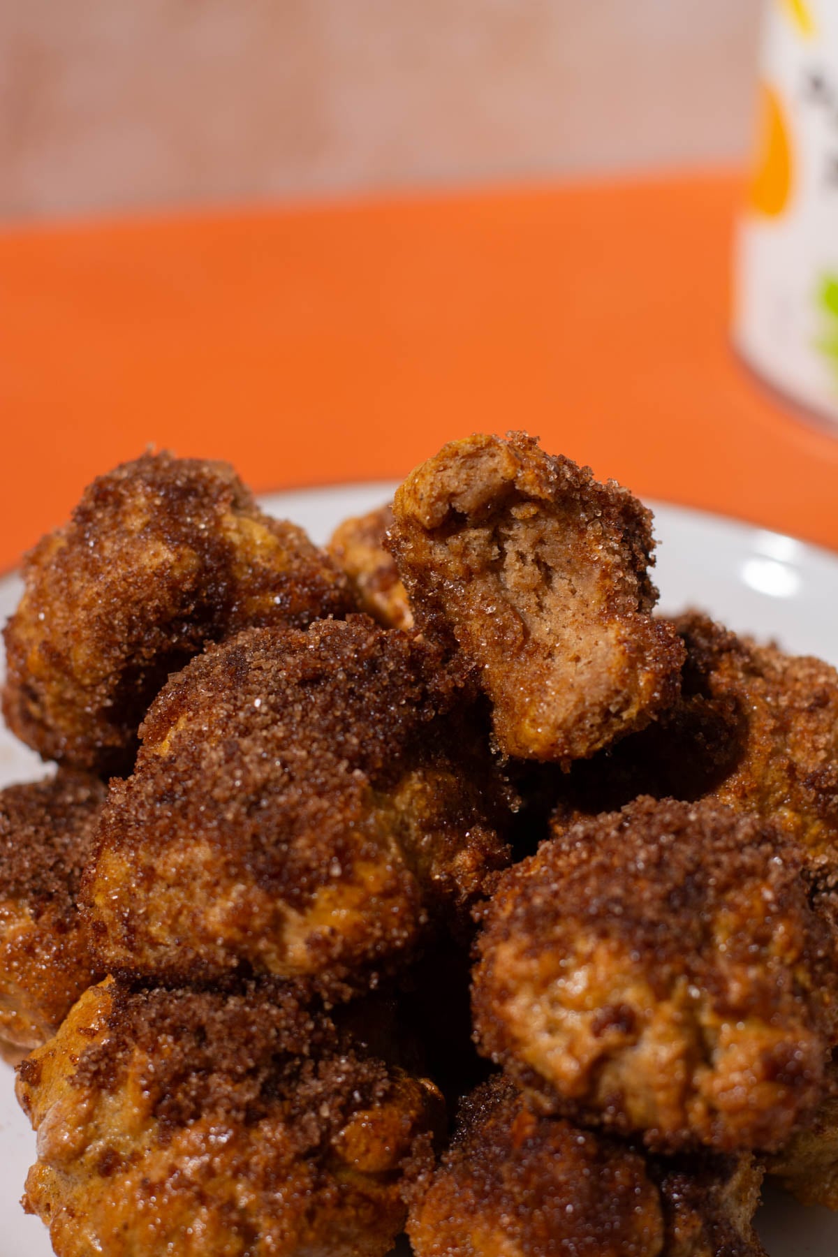 A plate of crispy, golden-brown fried meatballs piled high, perfect for a high-protein snack. One is bitten into, revealing the tender interior. The soft orange background hints at a patterned object, reminiscent of the warmth of freshly baked bagel bites.