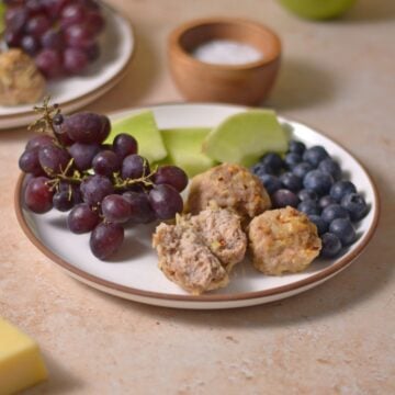 A white plate with breakfast meatballs, blueberries, grapes, and honeydew melon.